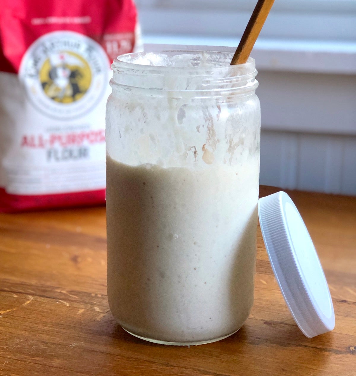 Discard sourdough starter in a jar, bag of King Arthur Flour in the back.