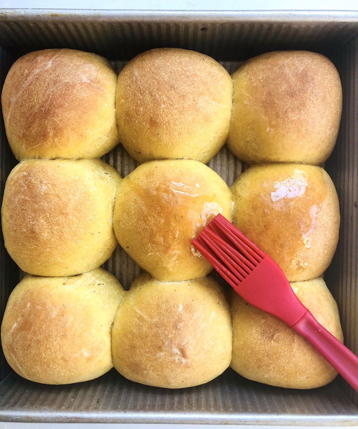 Baked pumpkin yeast rolls made with discard starter, being brushed with melted butter.
