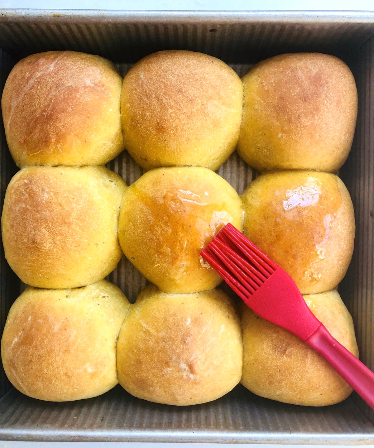 Baked pumpkin yeast rolls made with discard starter, being brushed with melted butter.