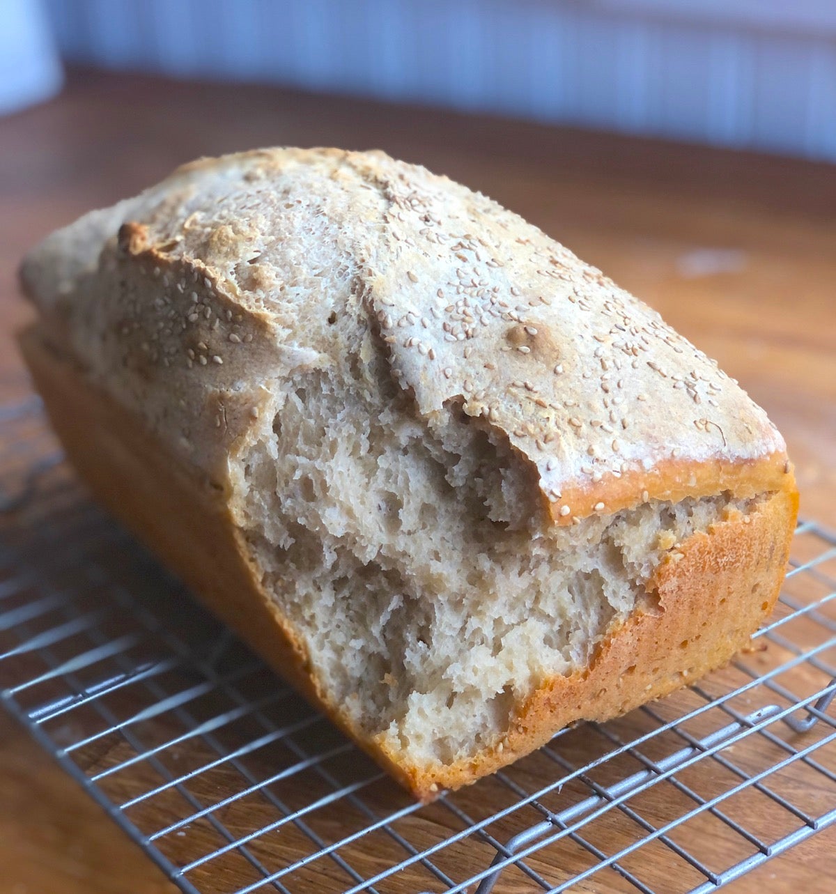 Loaf of bread on a cooling rack with one big chunk of corner torn off.