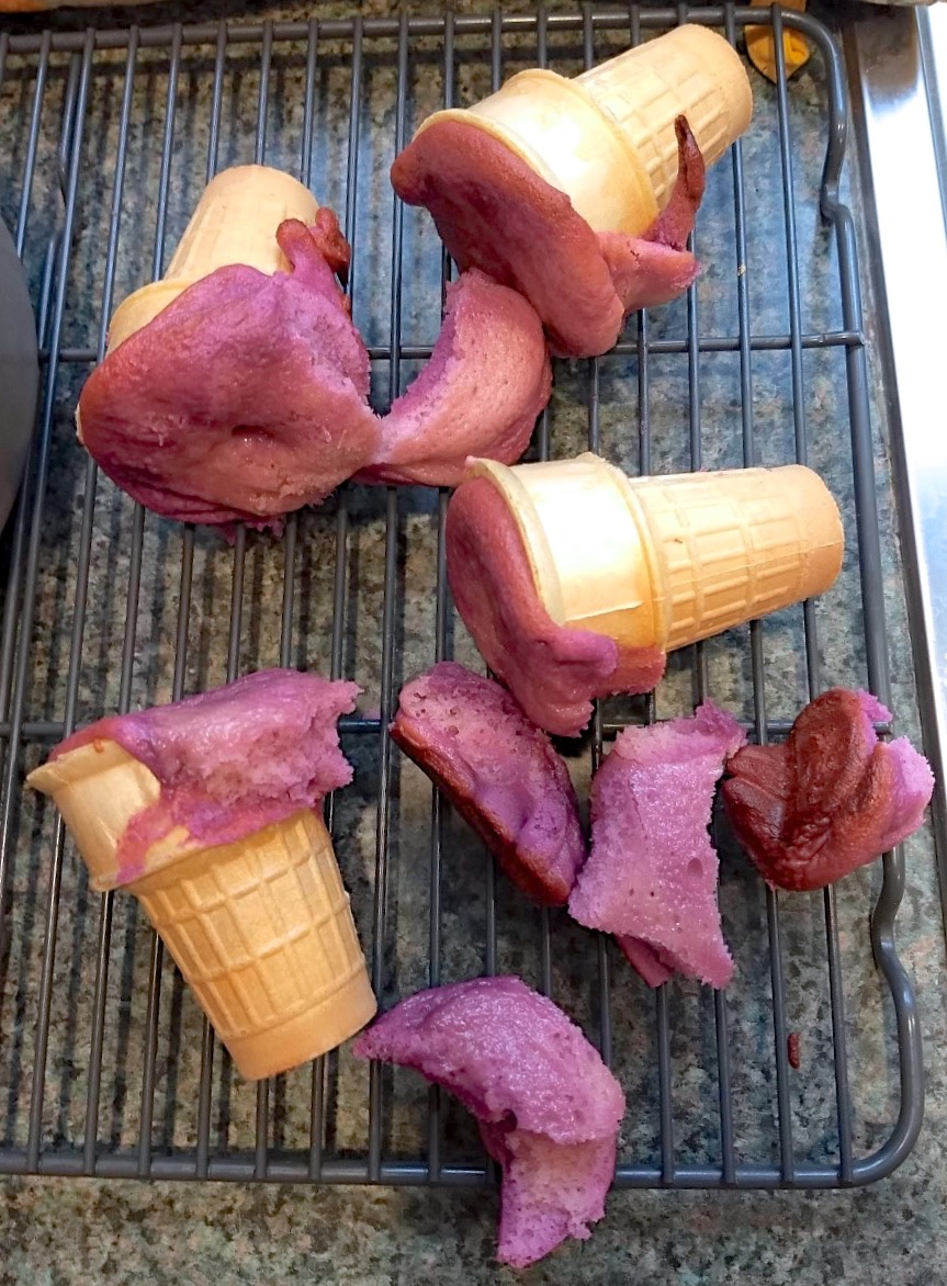 Fuchsia-colored cake batter  baked in cake-type ice cream cones, but severely overflowing the cones.