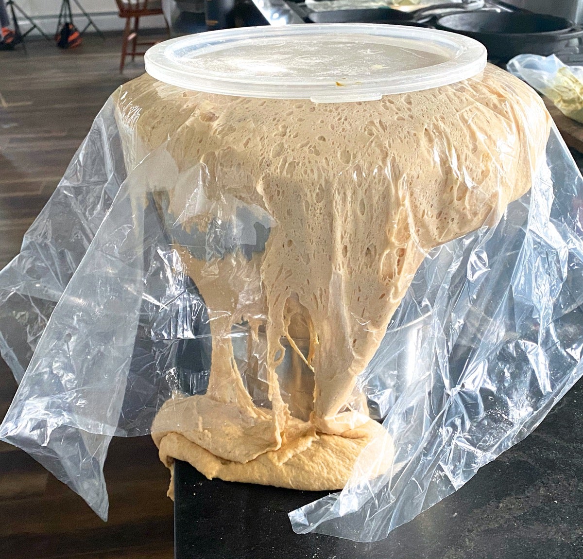 Whole wheat yeast dough overflowing its bowl and cascading onto the counter.