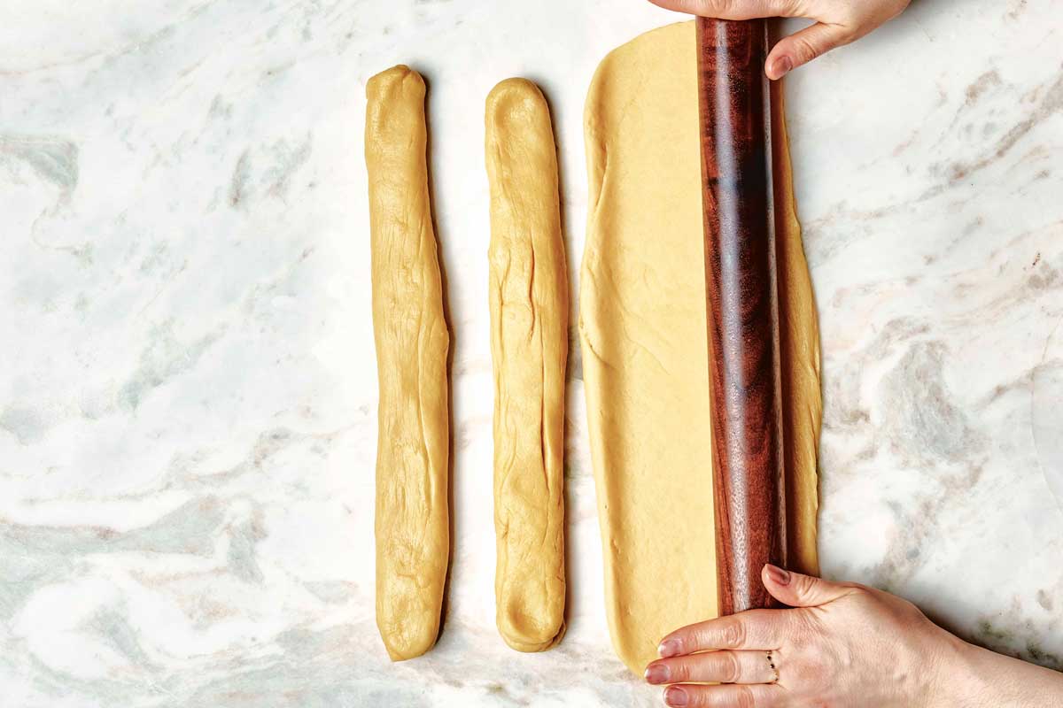 Hands rolling out one of three strands of dough