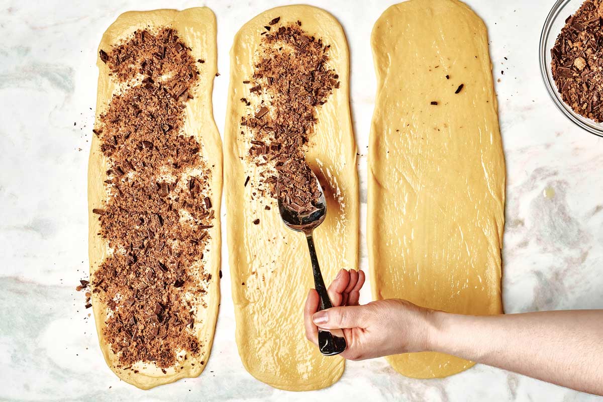 Hands using spoon to distribute filling on second of three rectangles of dough