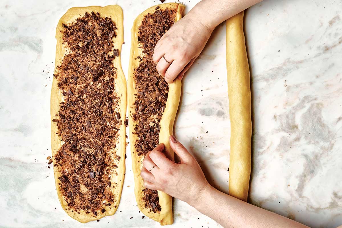 Rolling one strand on dough, next to a sealed shut log and unrolled rectangle of dough