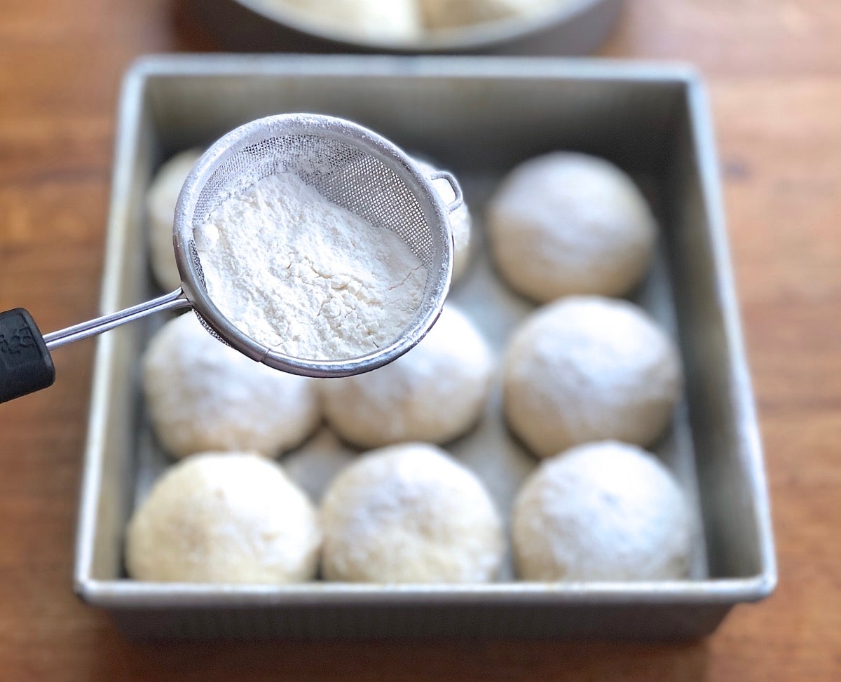 Oatmeal bread rolls being sprinkled with flour prior to baking to make snowflake rolls