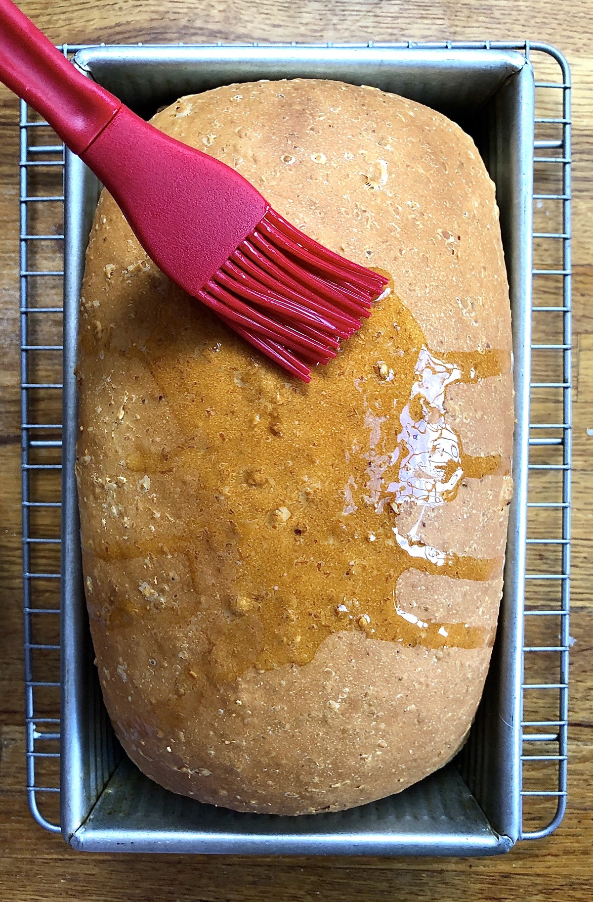 Oatmeal bread, hot out of the oven, being brushed with melted butter