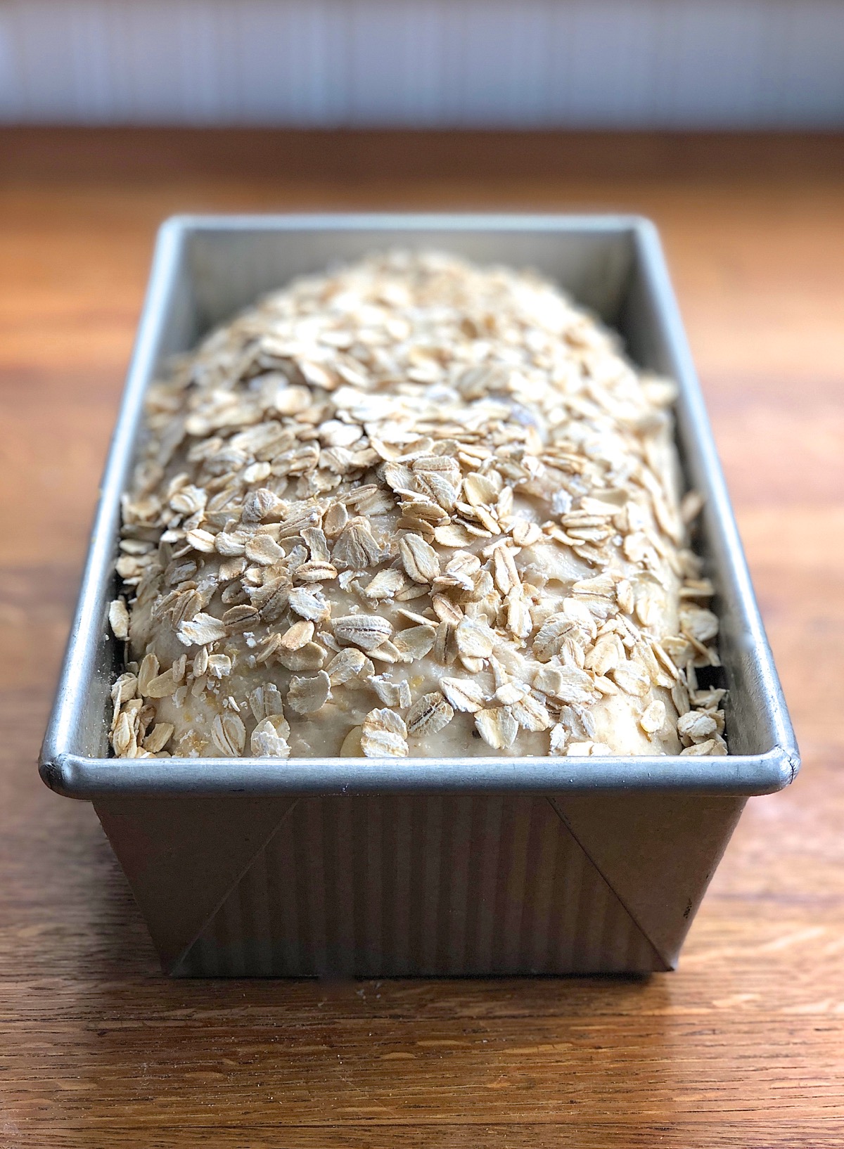 A garnish of oats sprinkled atop a risen loaf of oatmeal bread before baking
