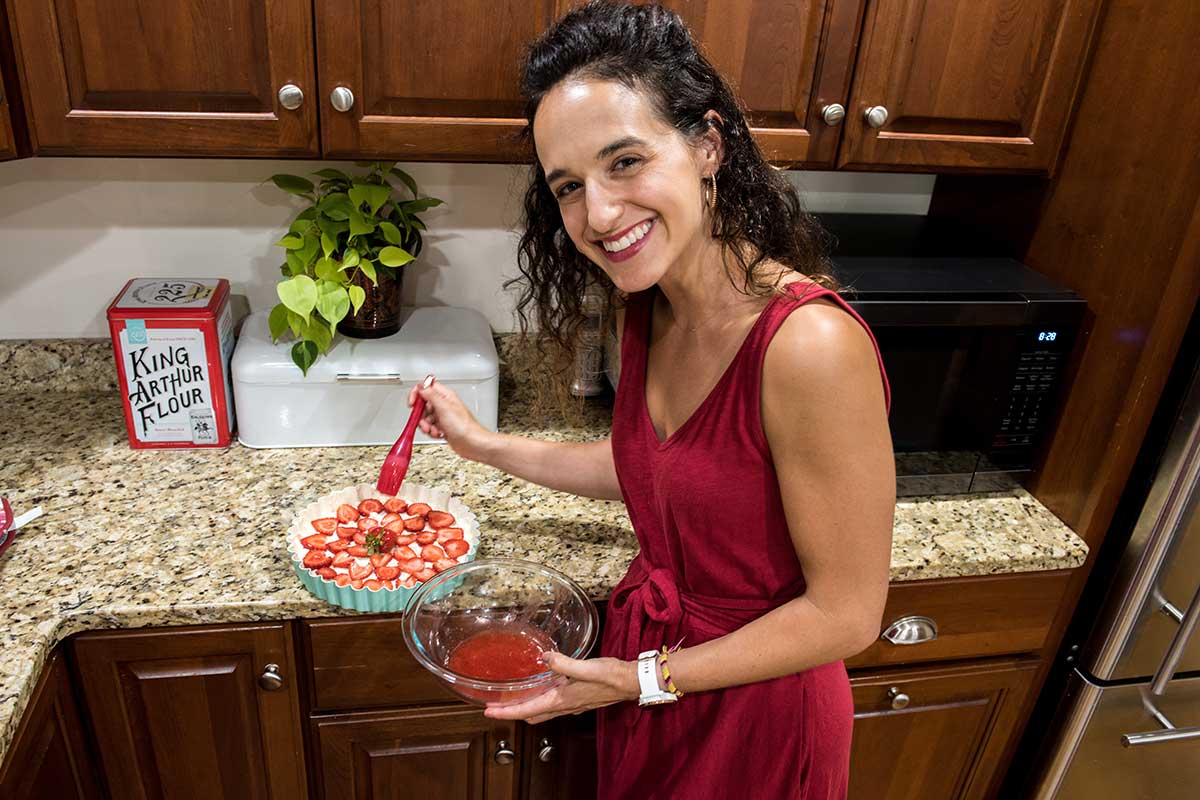 A woman in a red dress putting the finishing touches on a strawberry dessert in the kitchen