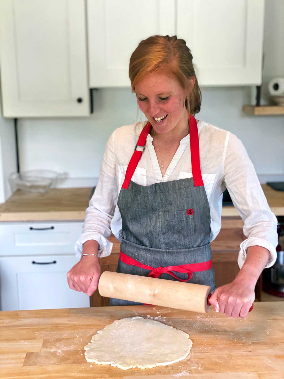 A woman with an apron on rolling out pie dough with a rolling  pin
