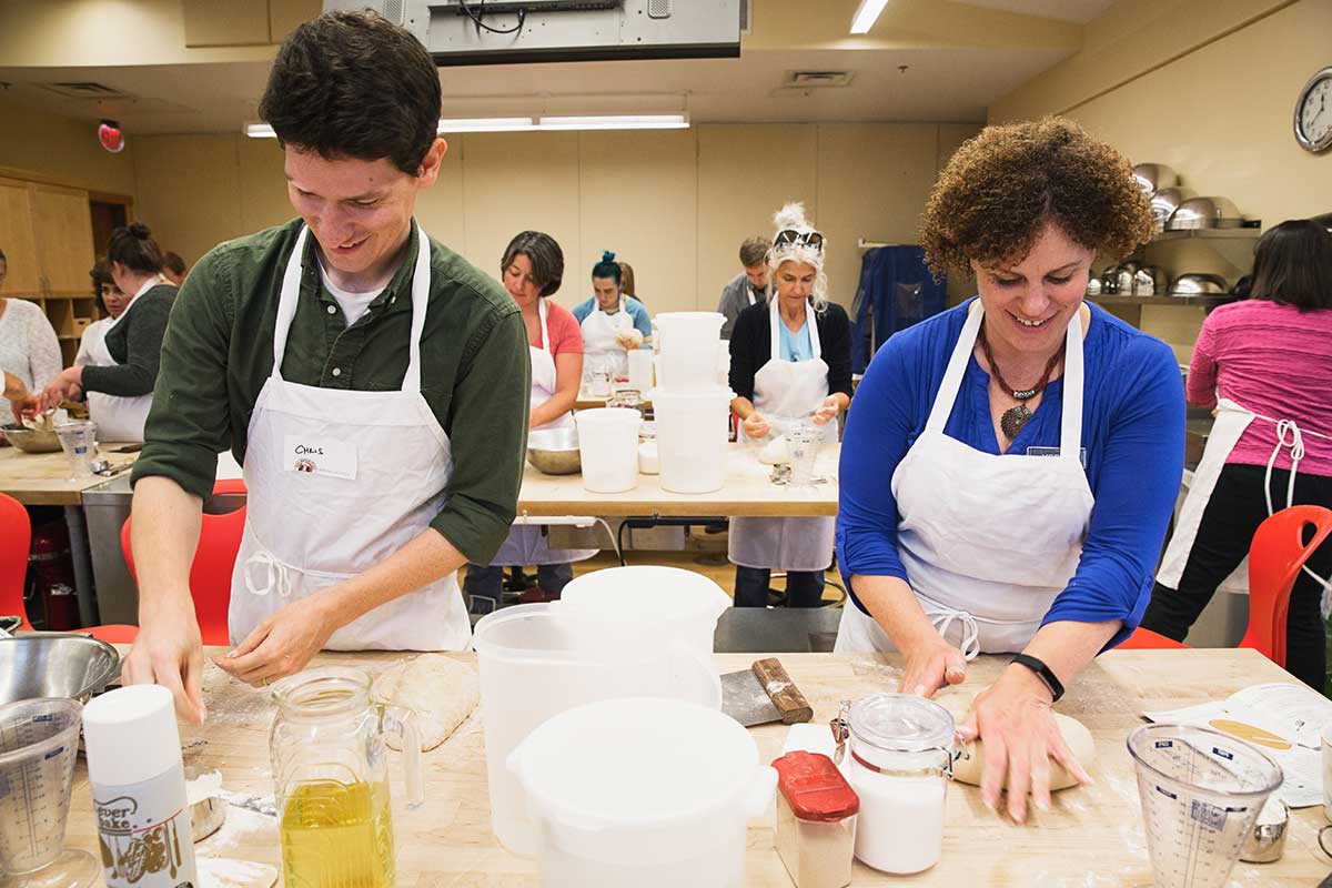 Two happy bakers wearing aprons kneading bread dough