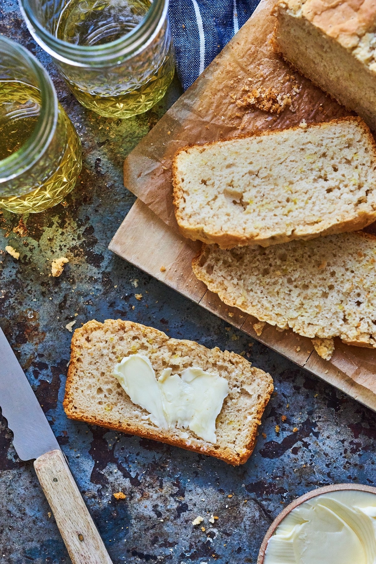 Loaf of beer bread sliced on a cutting board, one slice buttered.