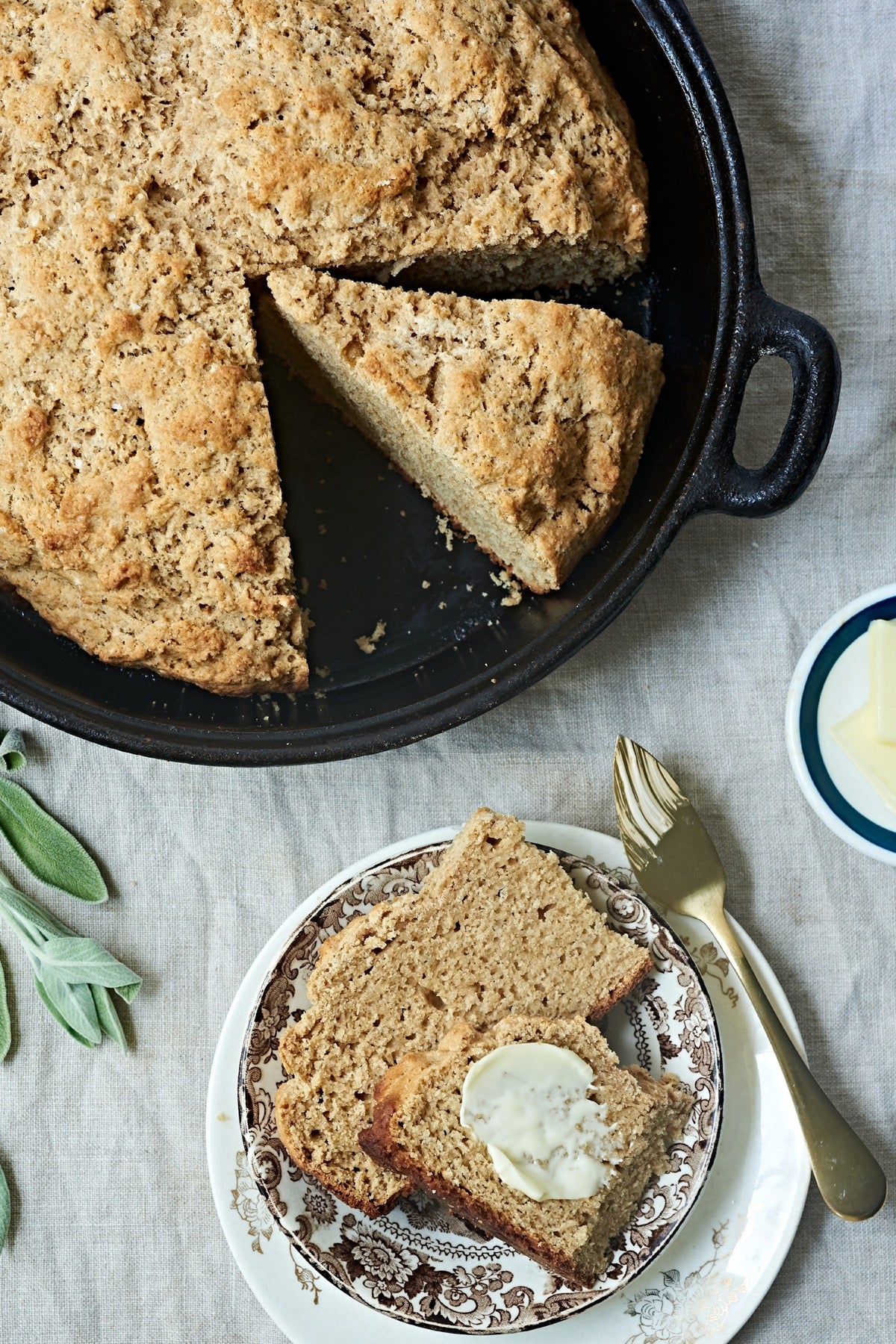 Irish Buttermilk Brown Bread baked in a cast iron pan, one wedge placed on a plate and buttered.