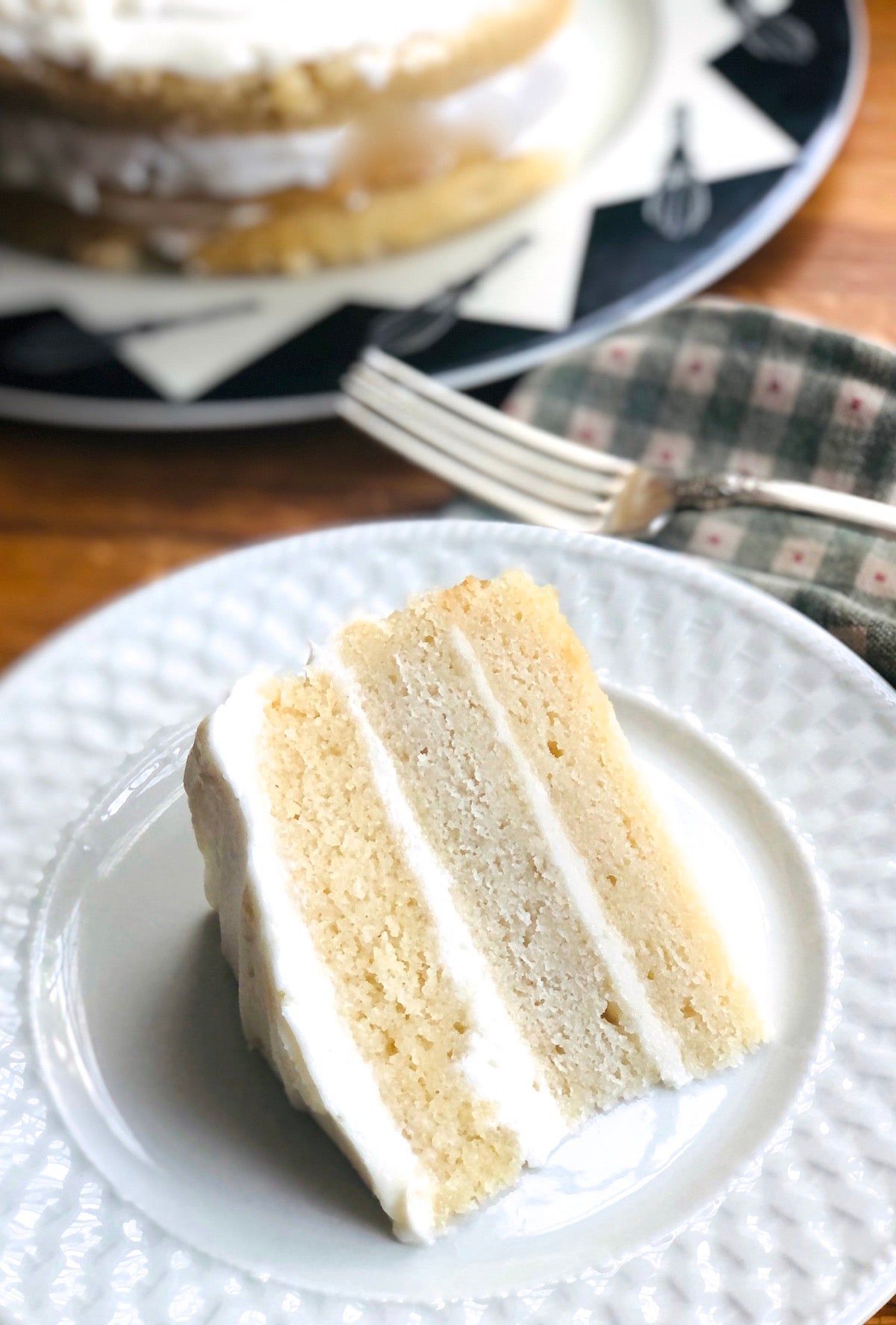 Slice of triple-layer vanilla cake with buttercream frosting on a plate, showing the different colors of the three layers, each made with a different type of butter.