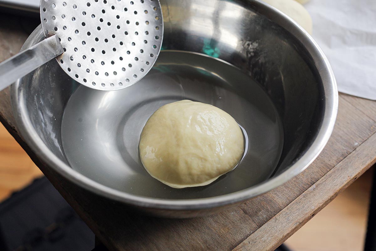 Bun being scooped from lye bath in stainless steel bowl