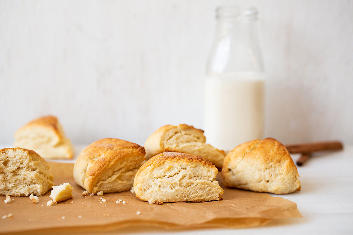 A pile of Cream Tea Scones on a kitchen table with a glass bottle of cream in the background