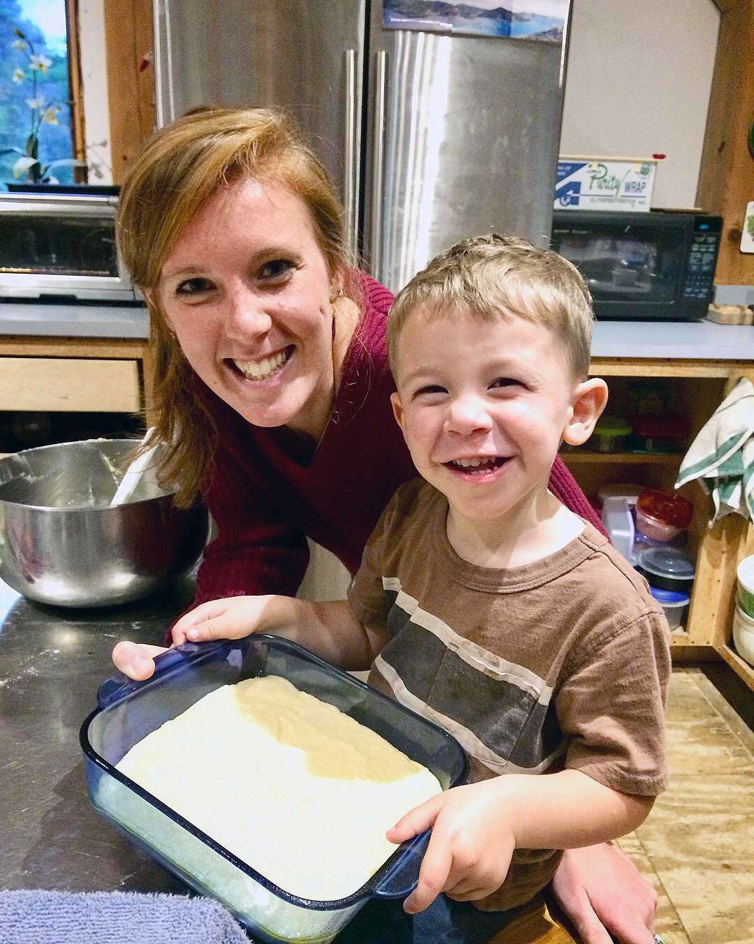 A woman standing next to a child who is smiling, holding up the cake they baked