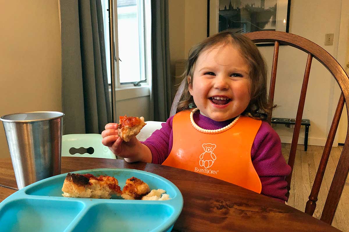 A small child enjoying a slice of crispy cheesy pan pizza with a big smile