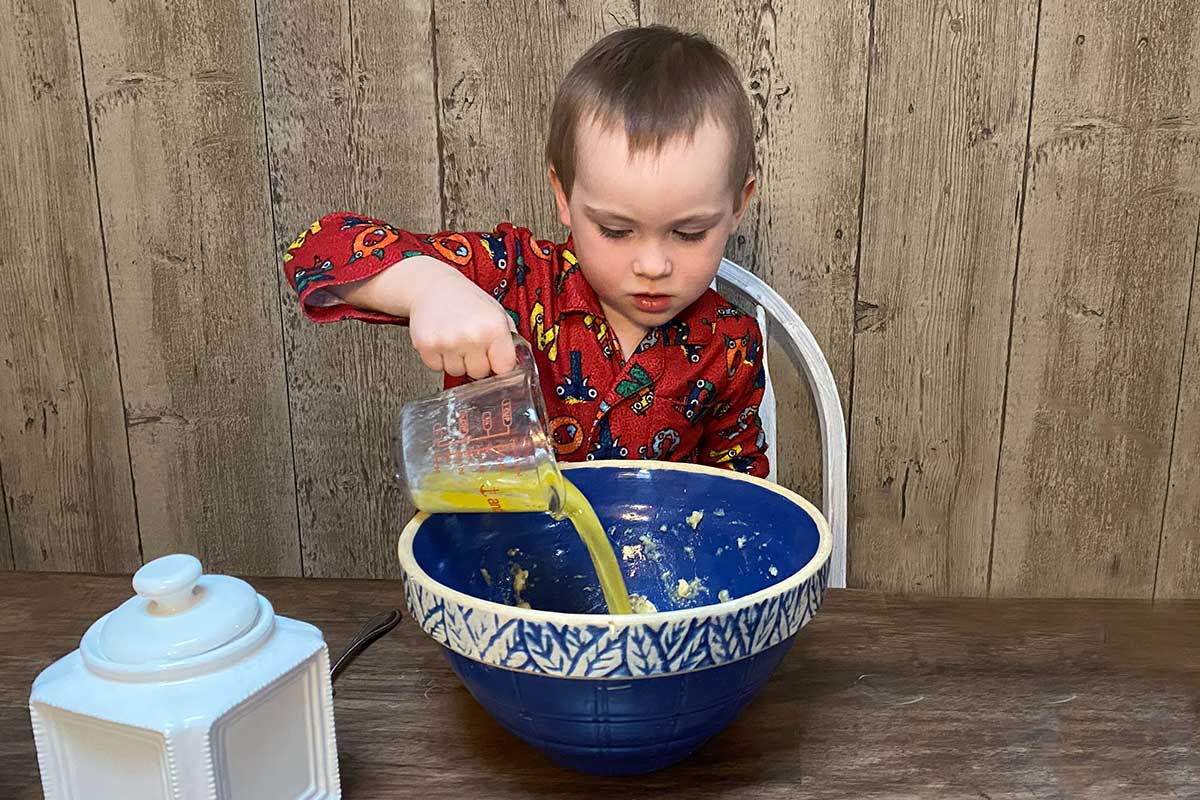 A small child baking blueberry muffins at home, adding orange juice to the batter