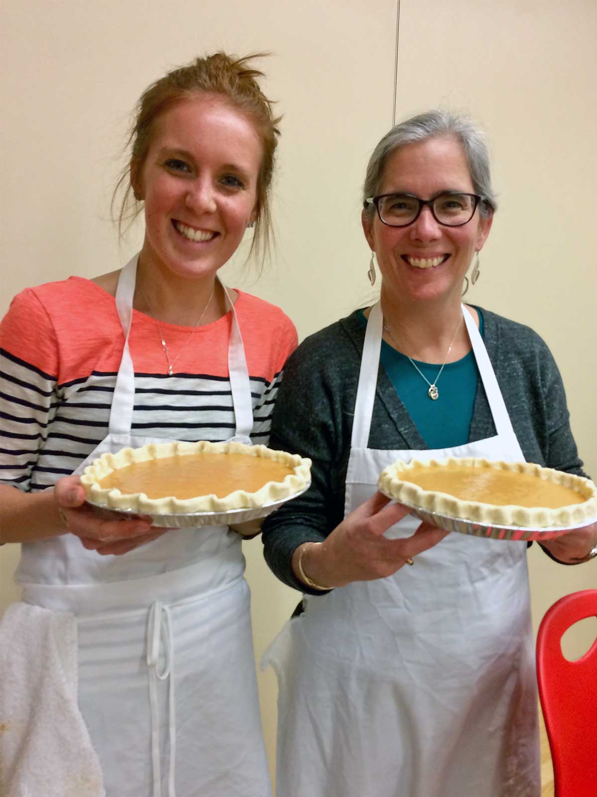 A mother and daughter standing side by side, holding pumpkin pies about to be baked