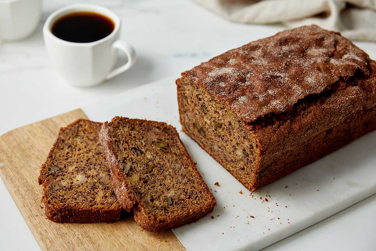 A loaf of banana bread on a wooden board with a few slices cut out of it