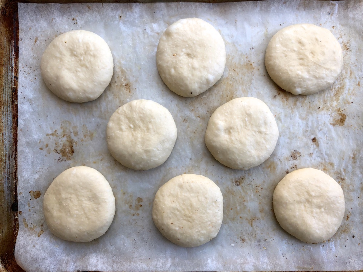 Eight round, flattened buns on a parchment-lined baking sheet.