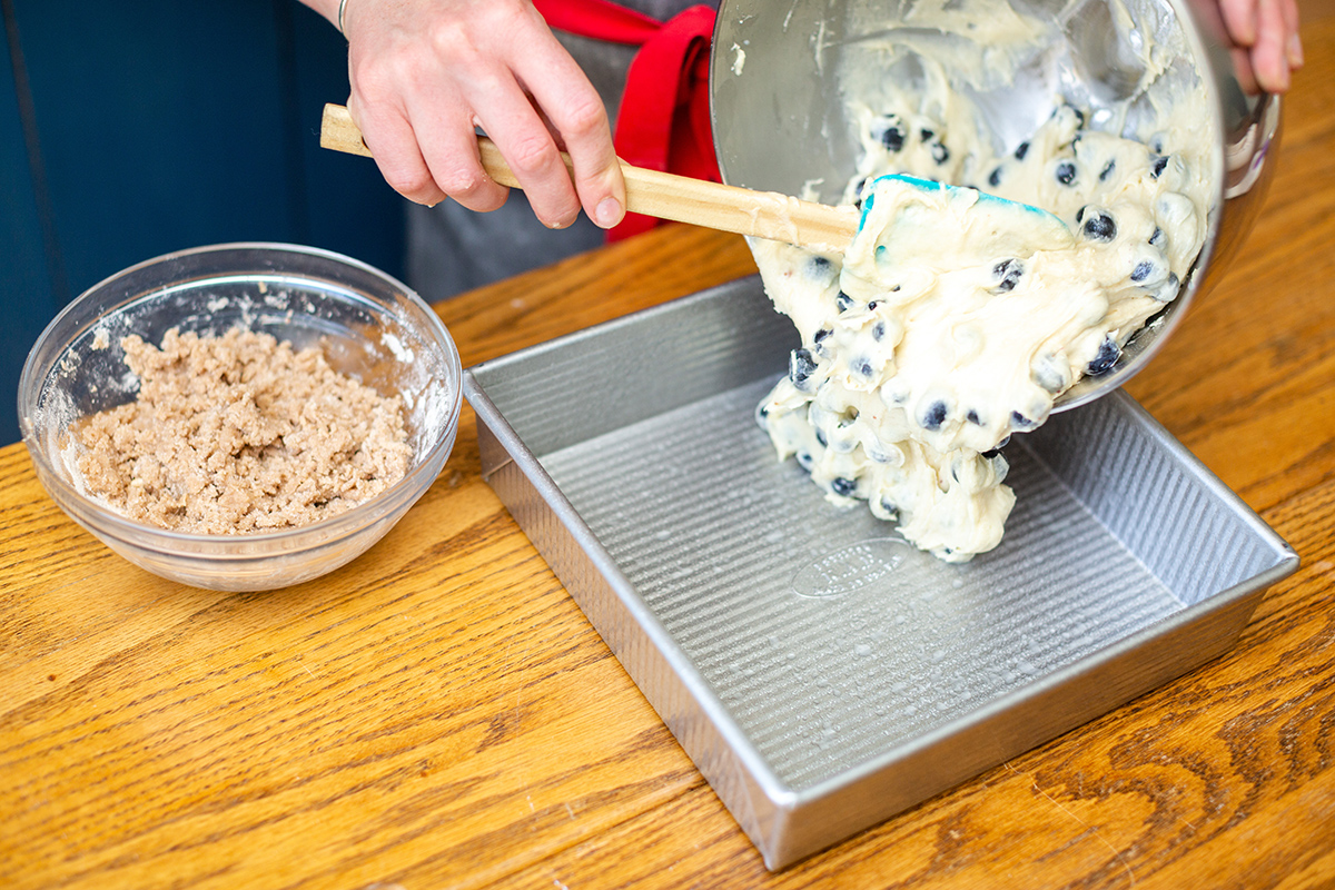 A baker pouring Blueberry Buckle Coffeecake batter into a prepared pan