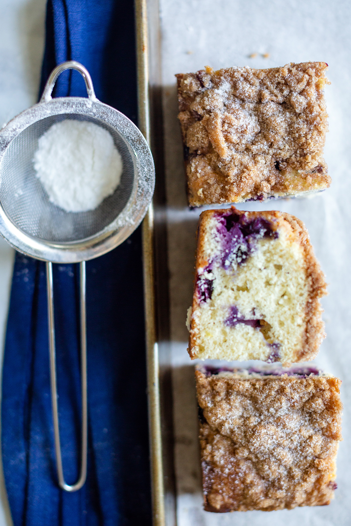 Three slices of Blueberry Buckle Coffeecake next to a sifter of confectioners' sugar