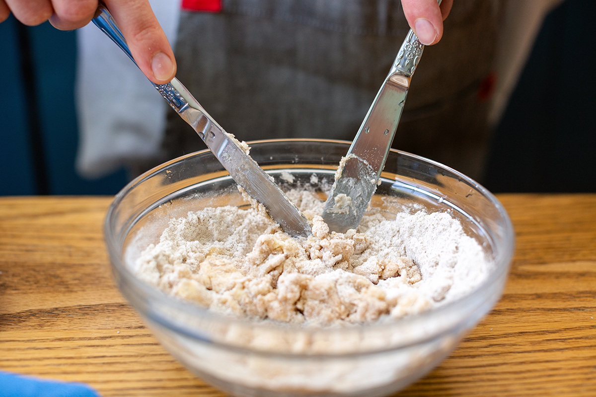 A baker using two knives to cut the butter into streusel topping ingredients