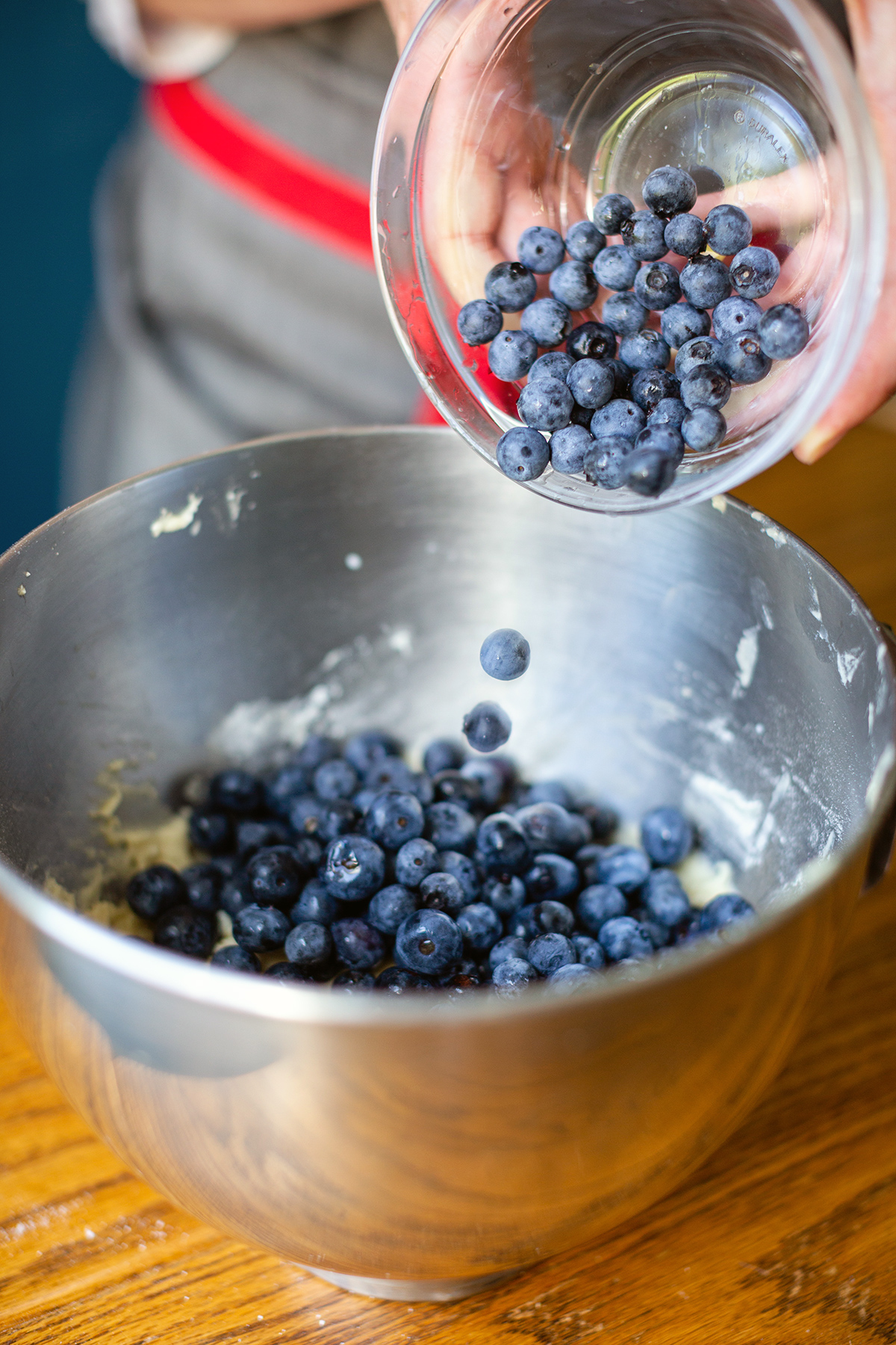 A baker pouring fresh blueberries into a mixing bowl of Blueberry Buckle Coffeecake batter