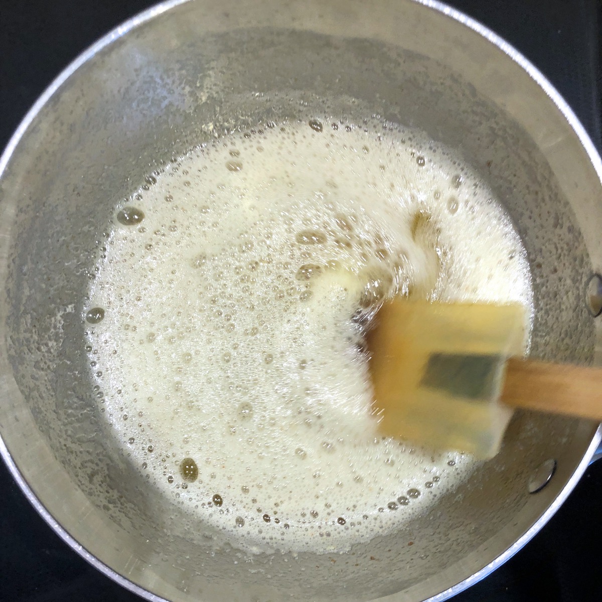 Using a spatula to stir simmering butter in a skillet.