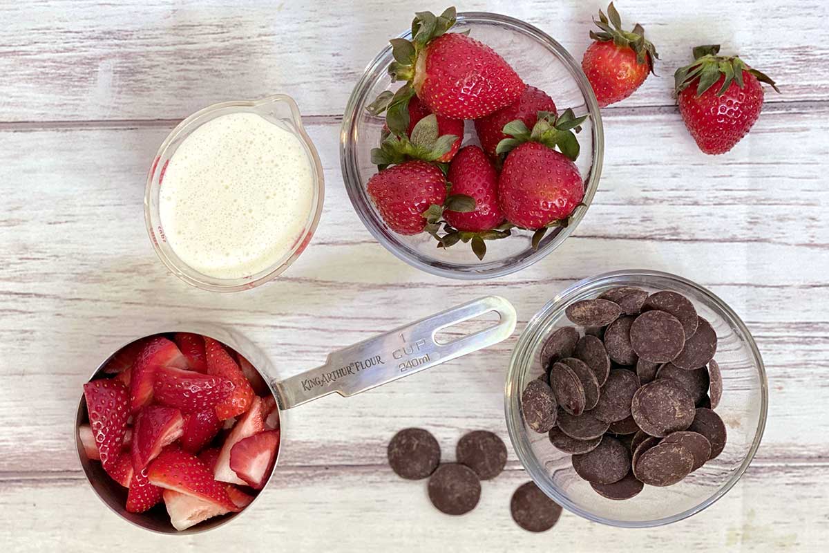 A bowl of fresh strawberries, chocolate, and cream on a kitchen table