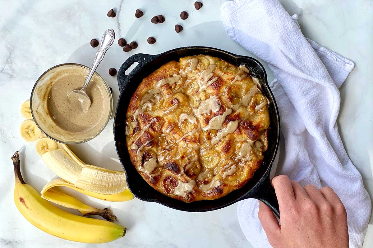 A brunch pizza in a cast iron pan topped with brown sugar, slices of banana, and nut butter