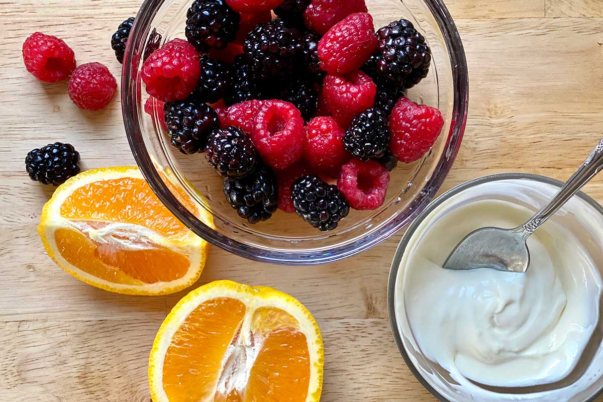 A bowl of fresh berries, orange slices, and mascarpone on a wooden table