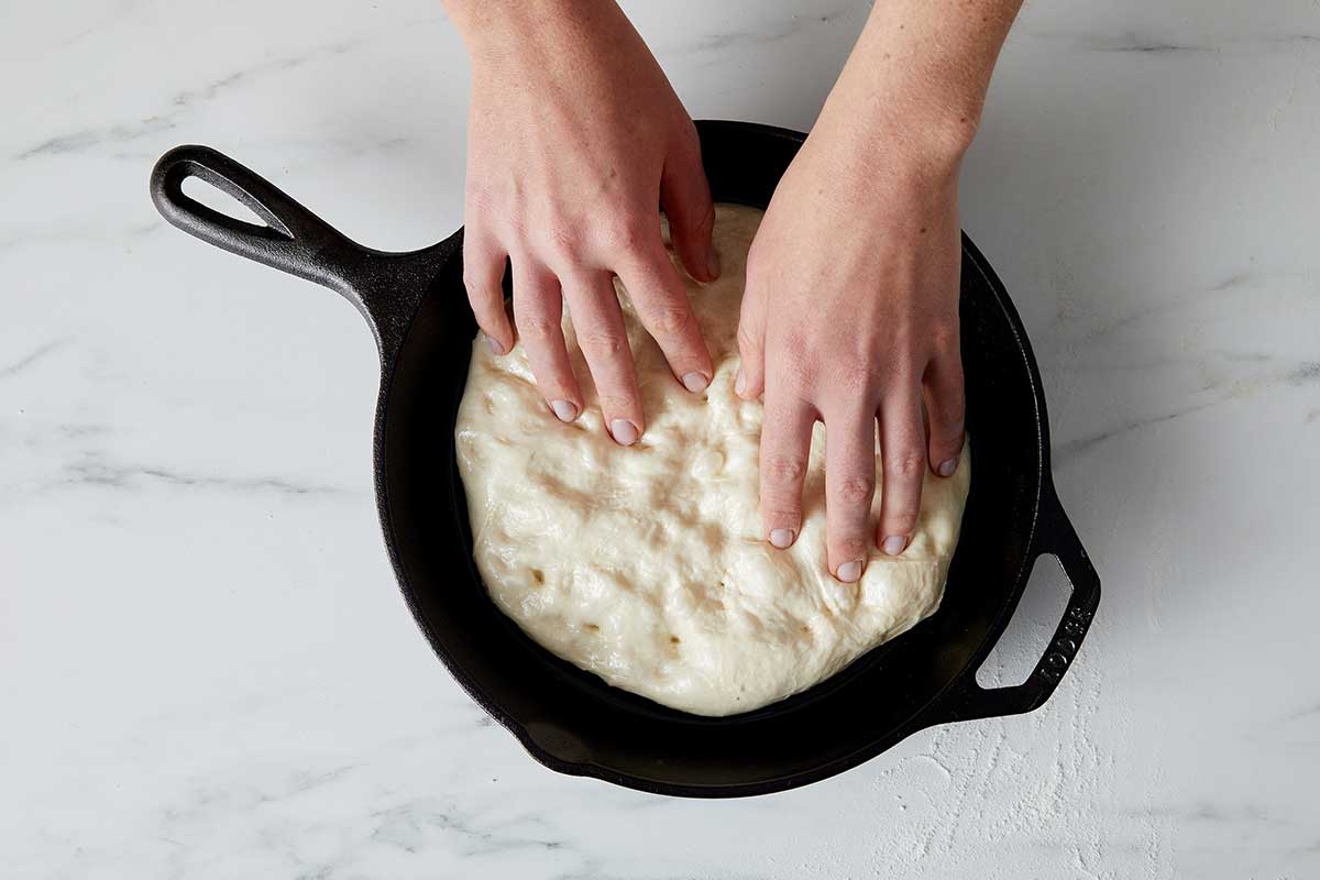 A baker spreading out dough in a cast iron pan