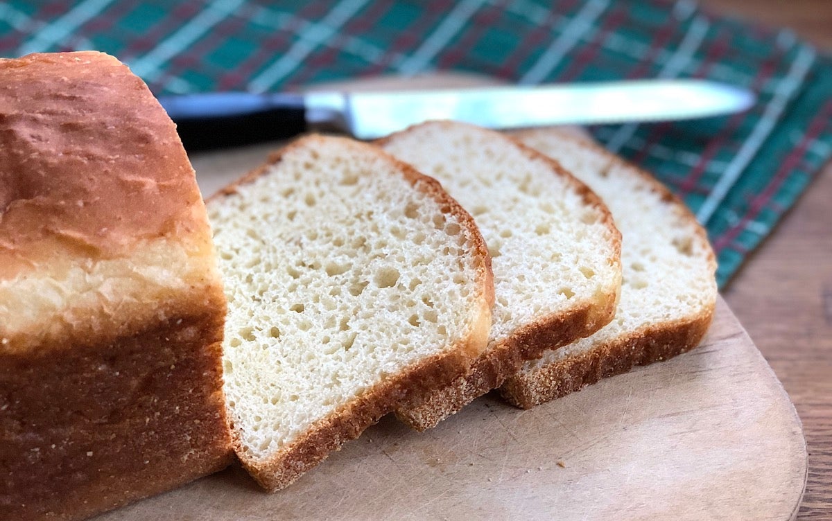 Loaf of bread on a cutting board with knife, three slices sliced.