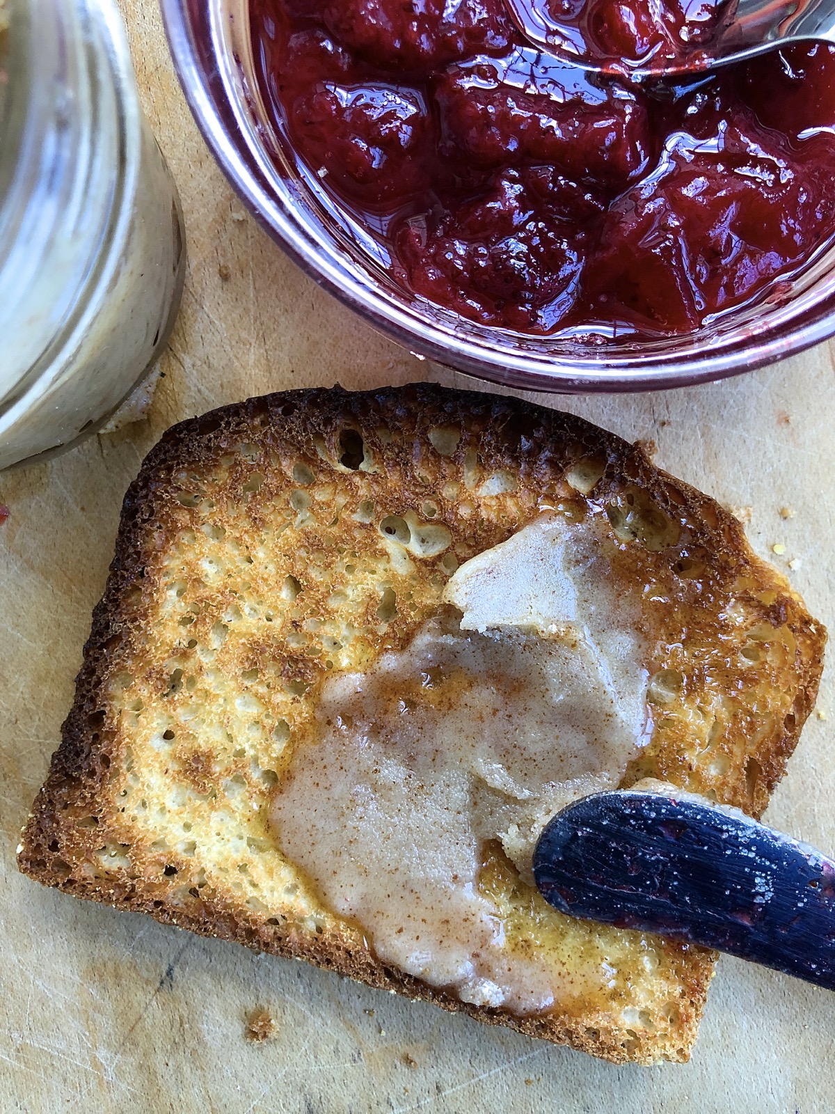Slice of buttered toast flanked by strawberry jam and brown butter.