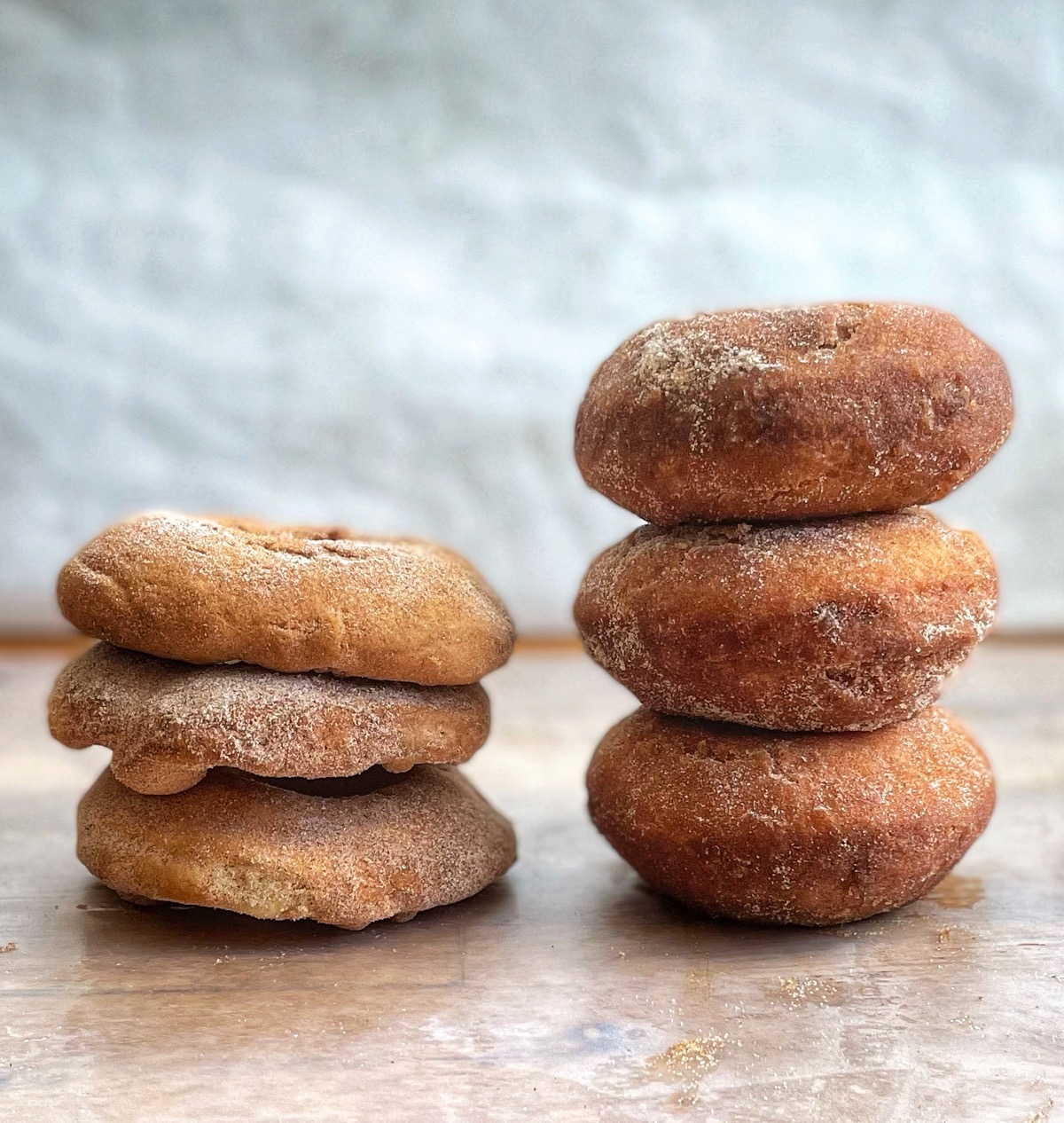 Stack of three doughnuts fried in hot oil next to a stack of three doughnuts cooked in an air fryer, showing how much less the air fryer doughnuts expand.