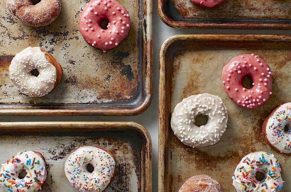 Yeast-raised doughnuts, colorfully frosted and decorated, arranged on a baking sheet. 