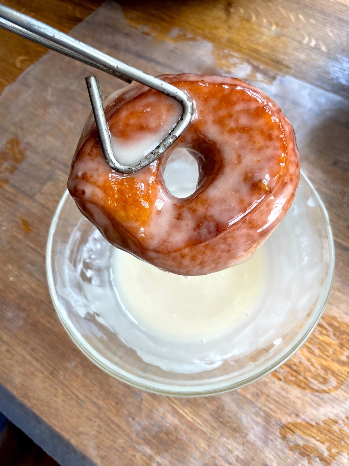 Yeast-raised doughnut fried in hot fat and being dipped in a clear sugar glaze.