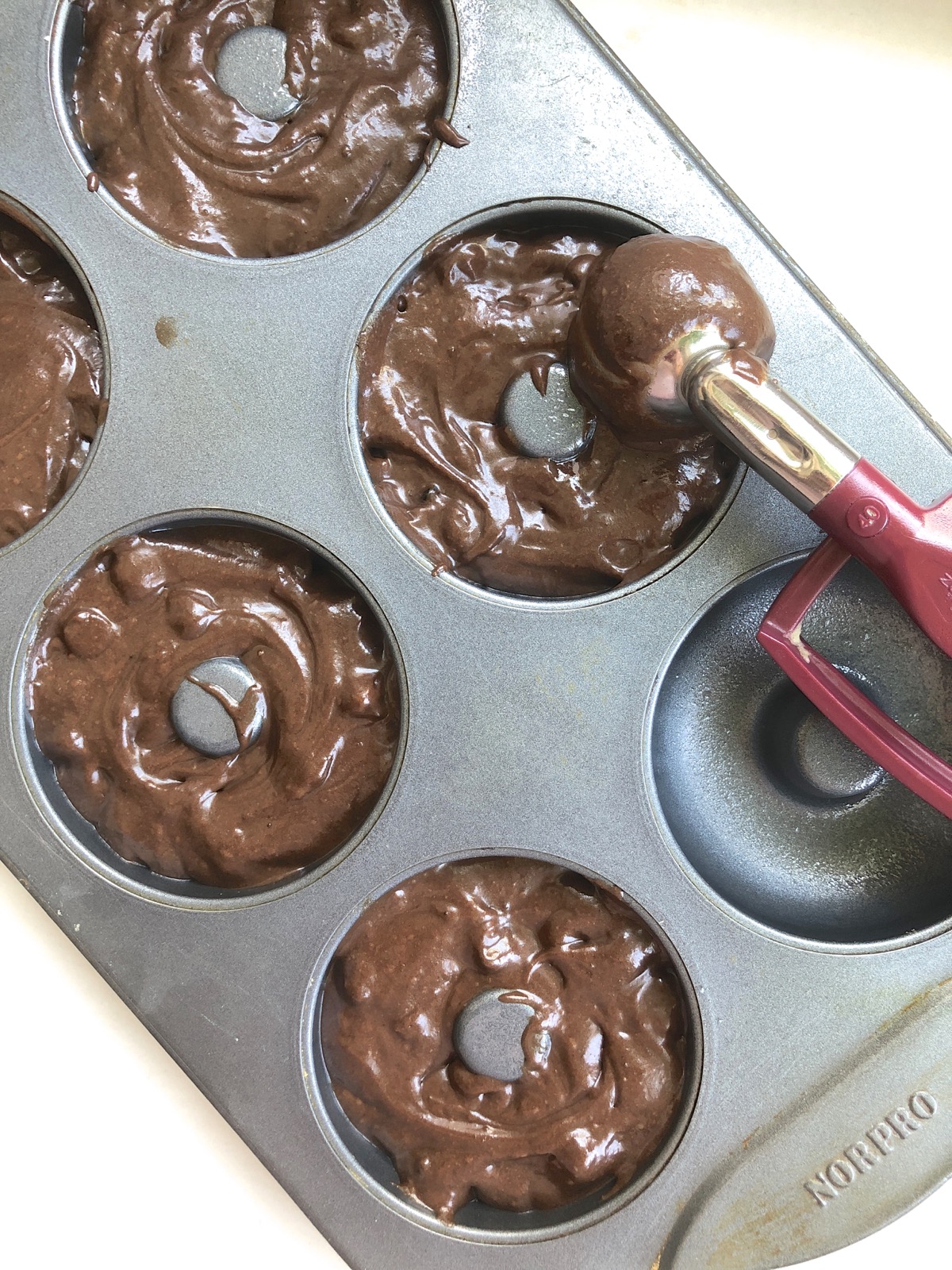 Chocolate doughnut batter scooped into doughnut pans using a cookie scoop.
