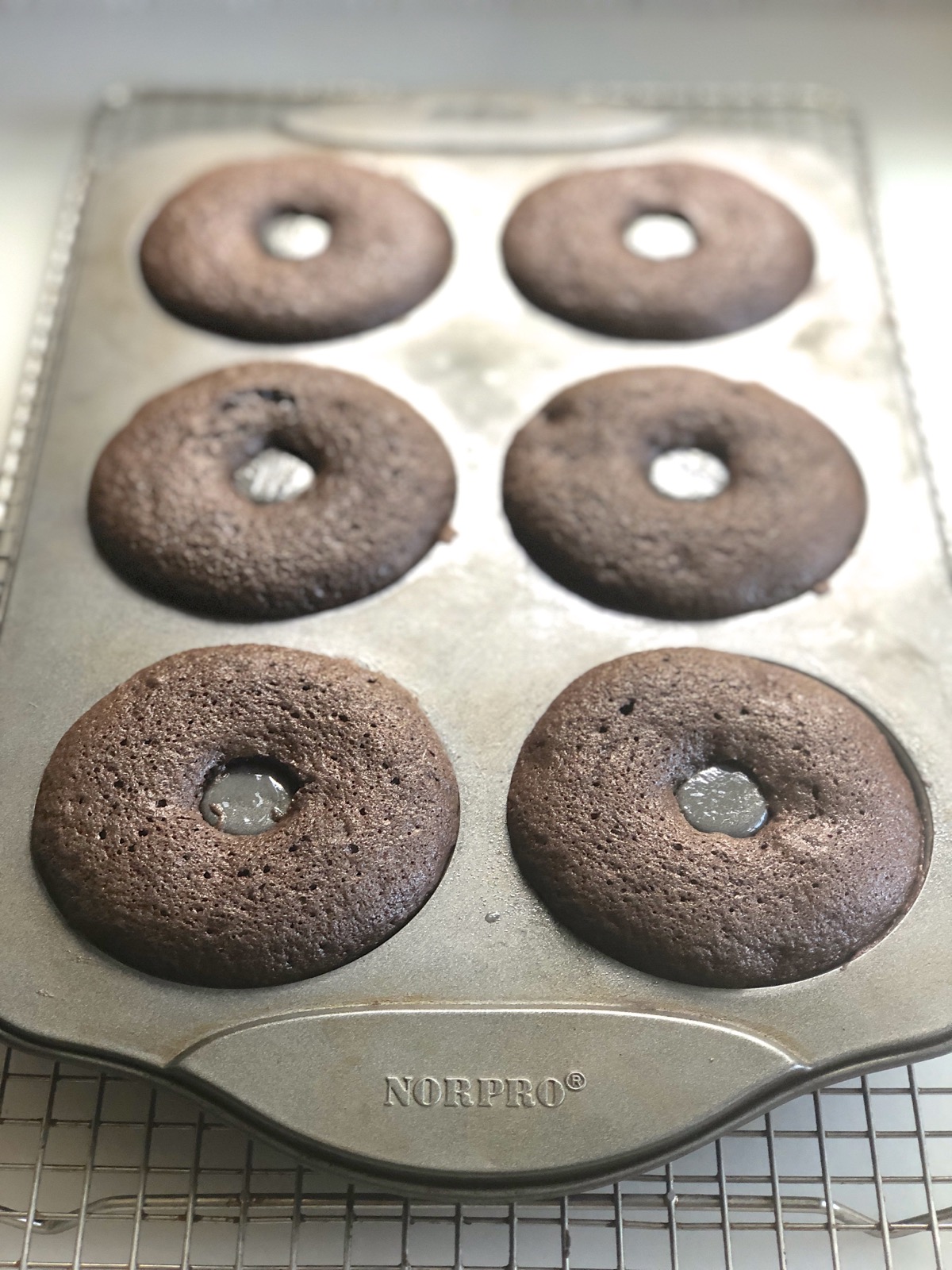 Chocolate doughnuts baked in a pan, resting on a cooling rack.