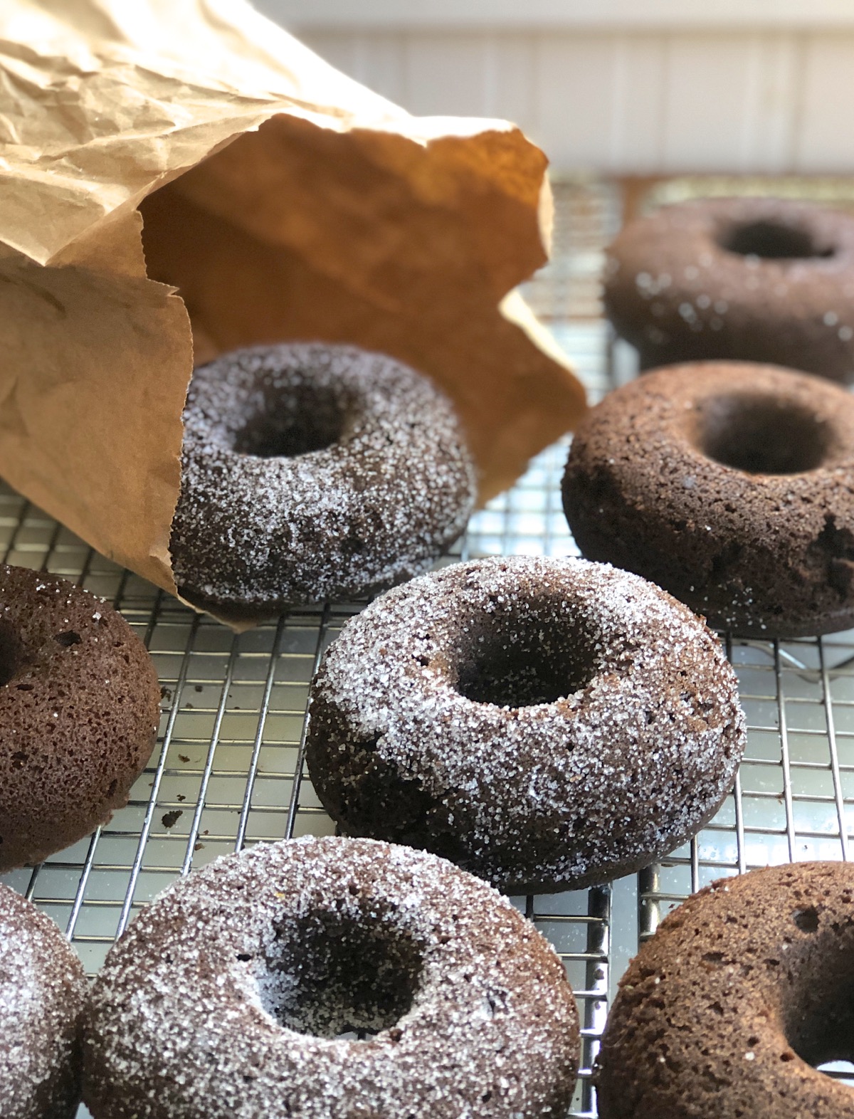 Chocolate doughnuts on a rack, one in paper bag with granulated sugar for shaking.