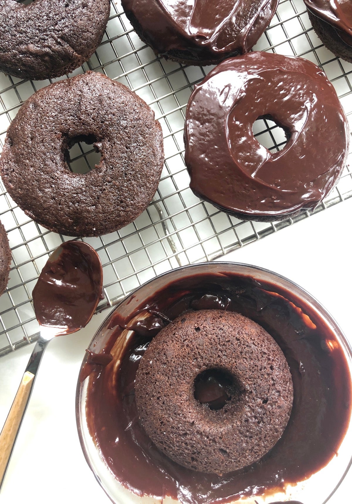 Chocolate doughnut being dipped in fudge icing, others with icing being spread.