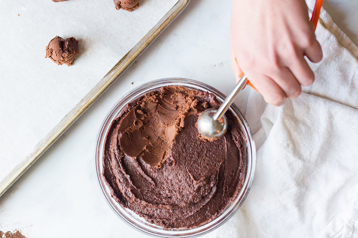 A baker scooping Chocolate Crinkle cookie dough from a mixing bowl using a cookie scoop