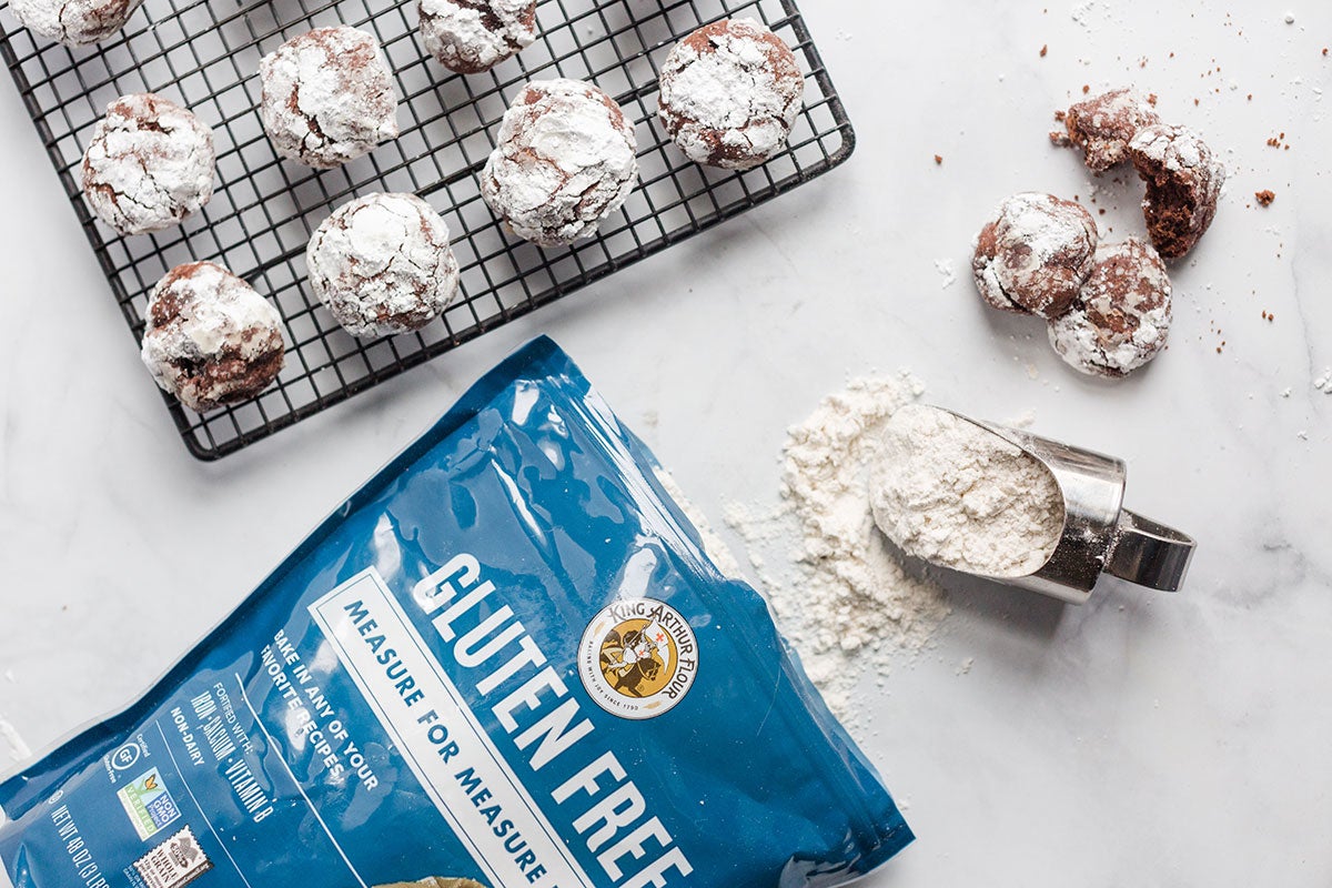 A few Gluten-Free Chocolate Crinkles on a cooling rack next to a bag of King Arthur Gluten-Free Measure for Measure Flour