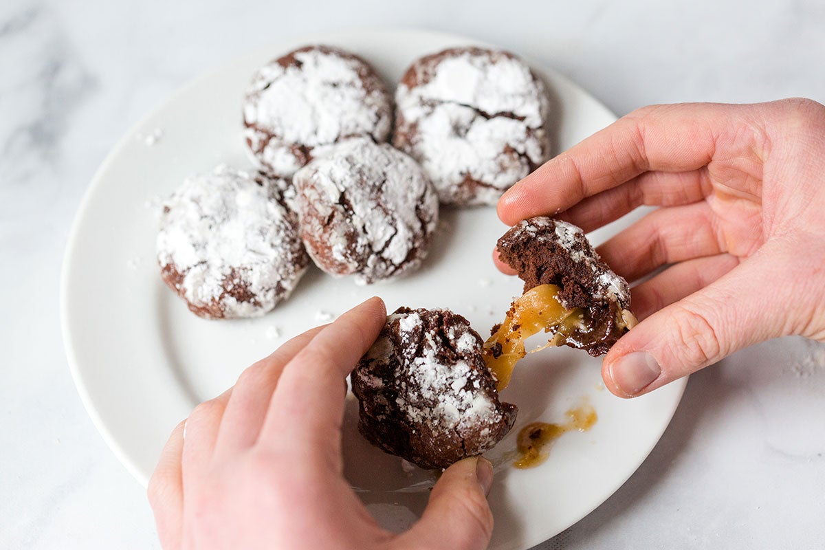 A baker breaking open a Chocolate Crinkle to reveal caramel inside