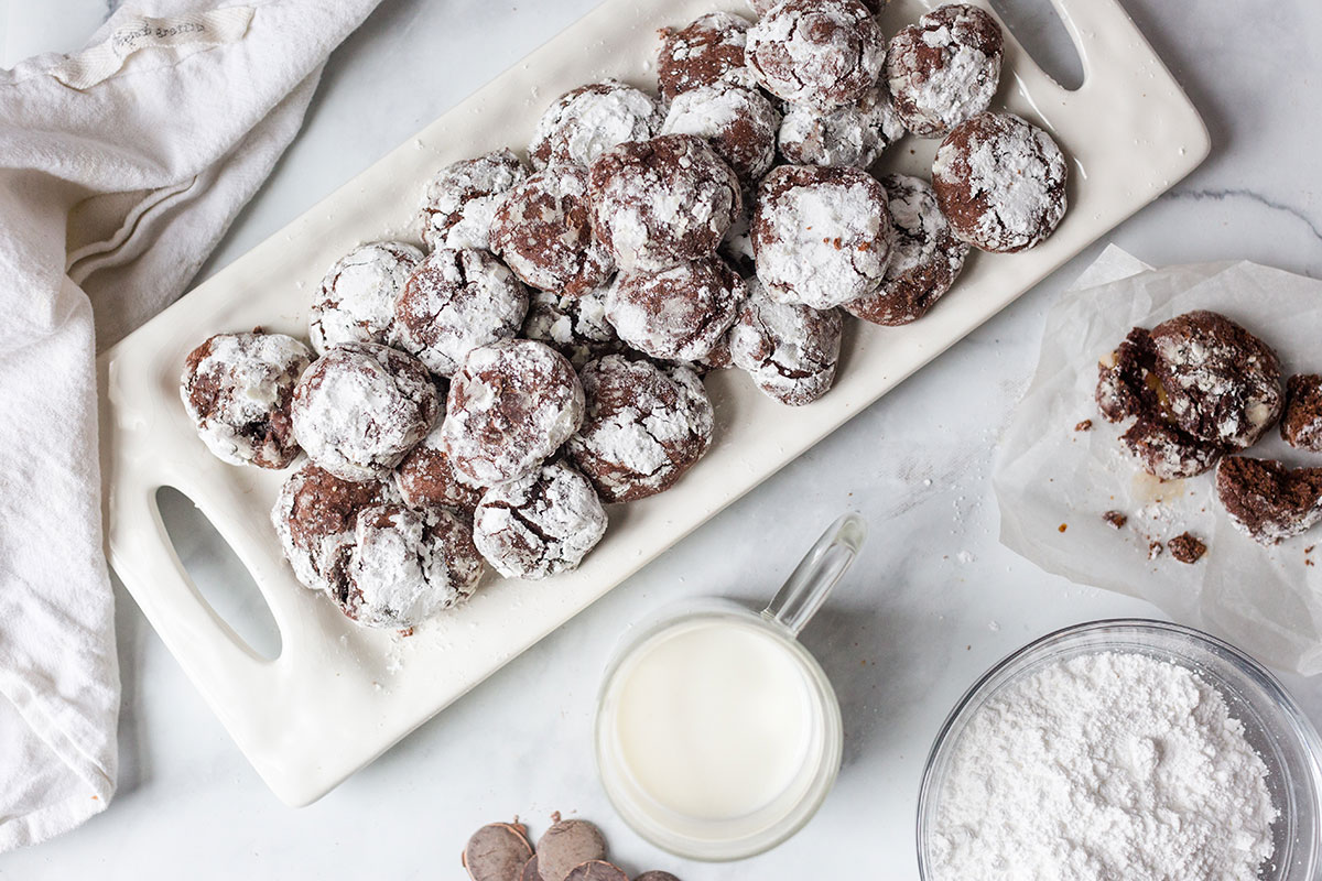 A platter of chocolate crinkles next to a cup of milk on a table