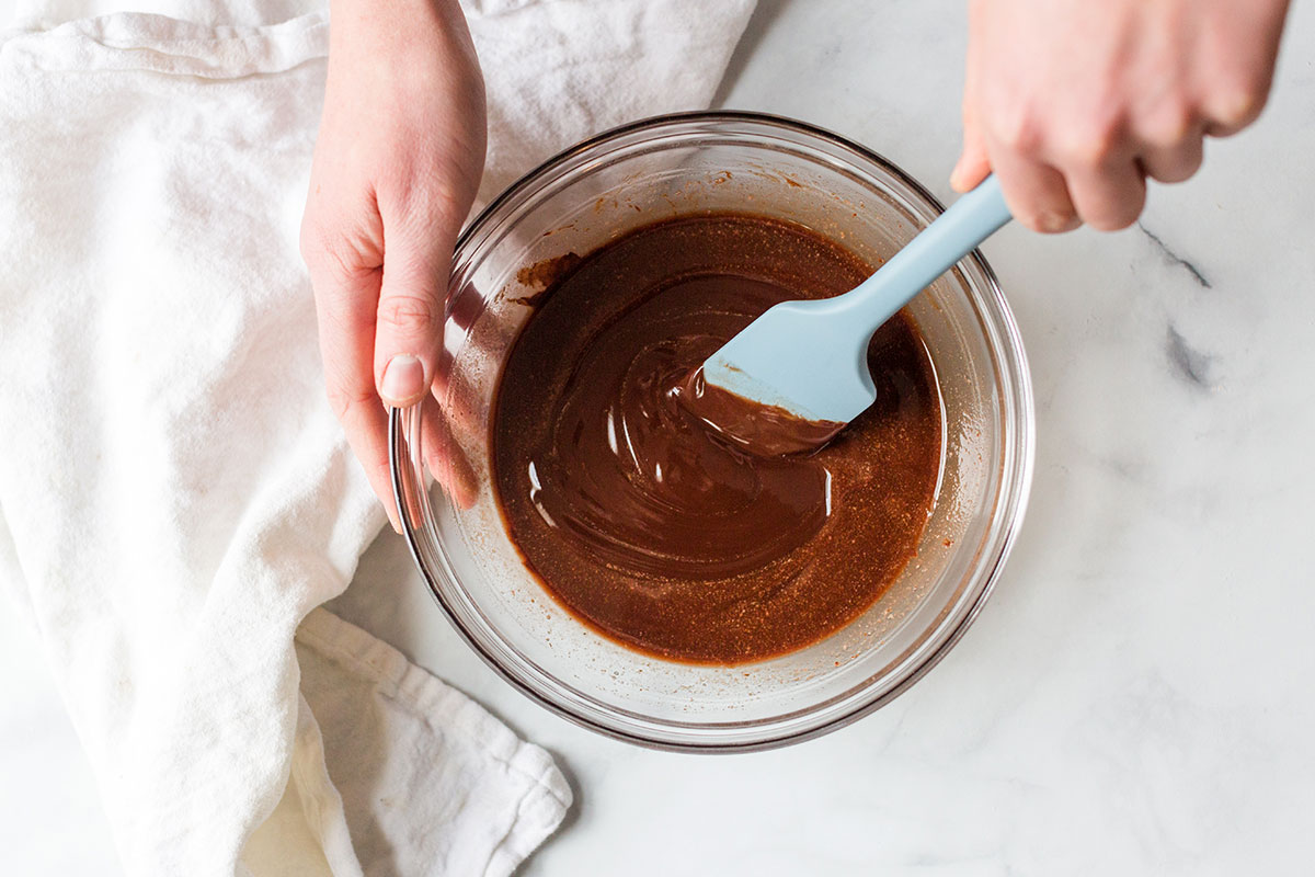 A baker mixing together melted chocolate and butter in a bowl with a spatula