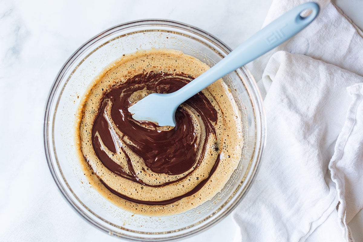 A mixing bowl with melted chocolate and butter that's partially mixed with beaten eggs and sugar